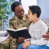 African american mother and son wearing soldier uniform reading book at home