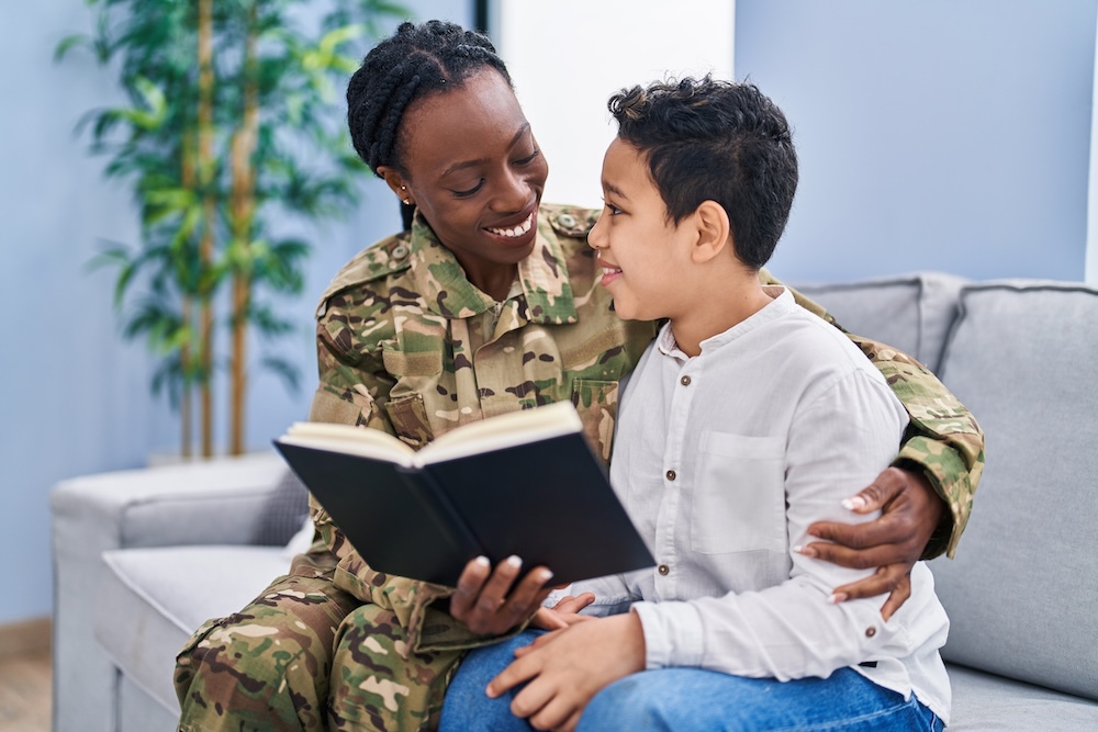 African american mother and son wearing soldier uniform reading book at home